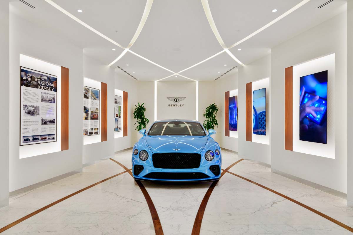 Picture of a bright-blue Bentley in a long hallway. The walls are adorned by motion graphics. Behind the car is the Bentley logo. 