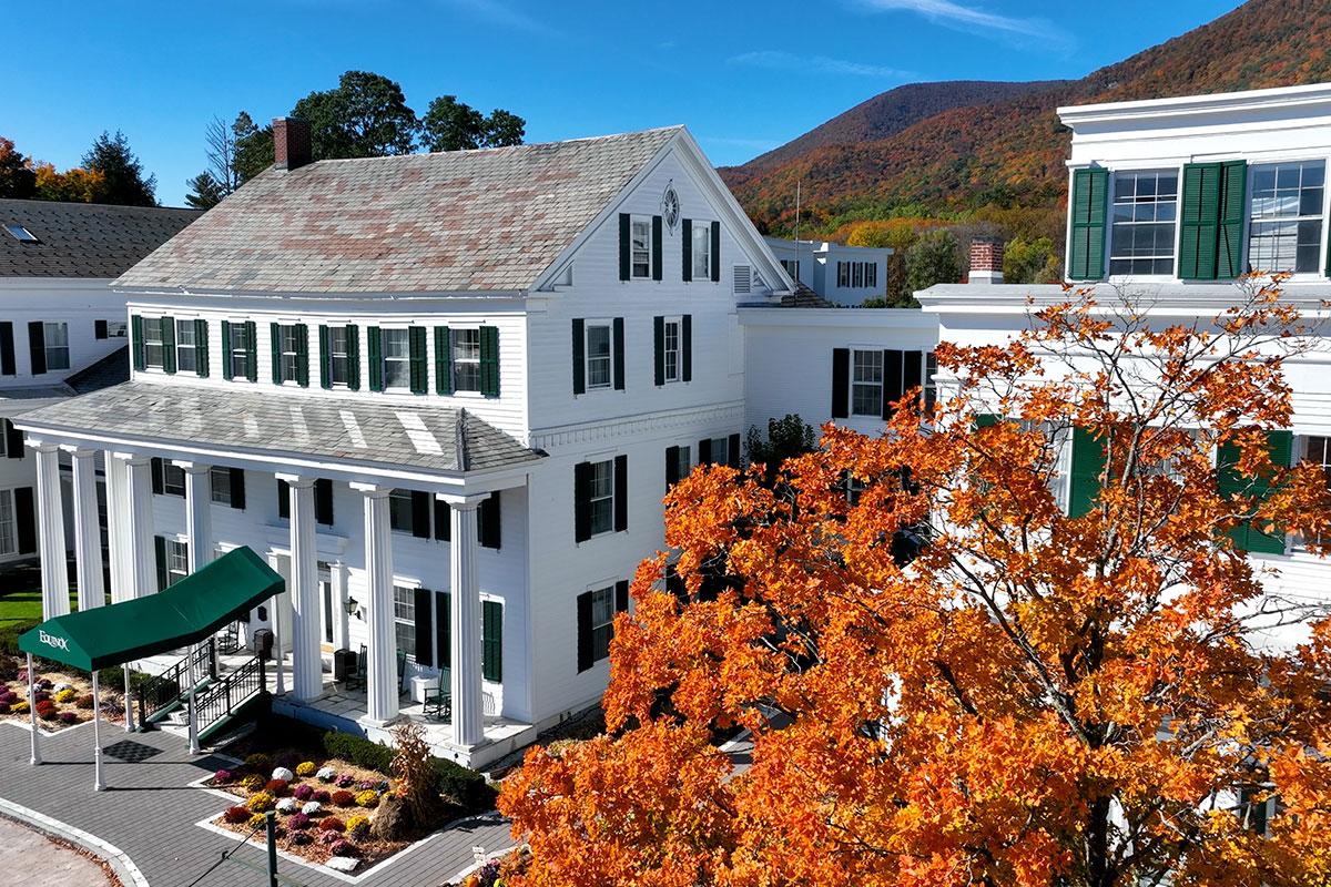 Gorgeous white four-story home at The Equinox, next to a tree with orange fall leaves. 