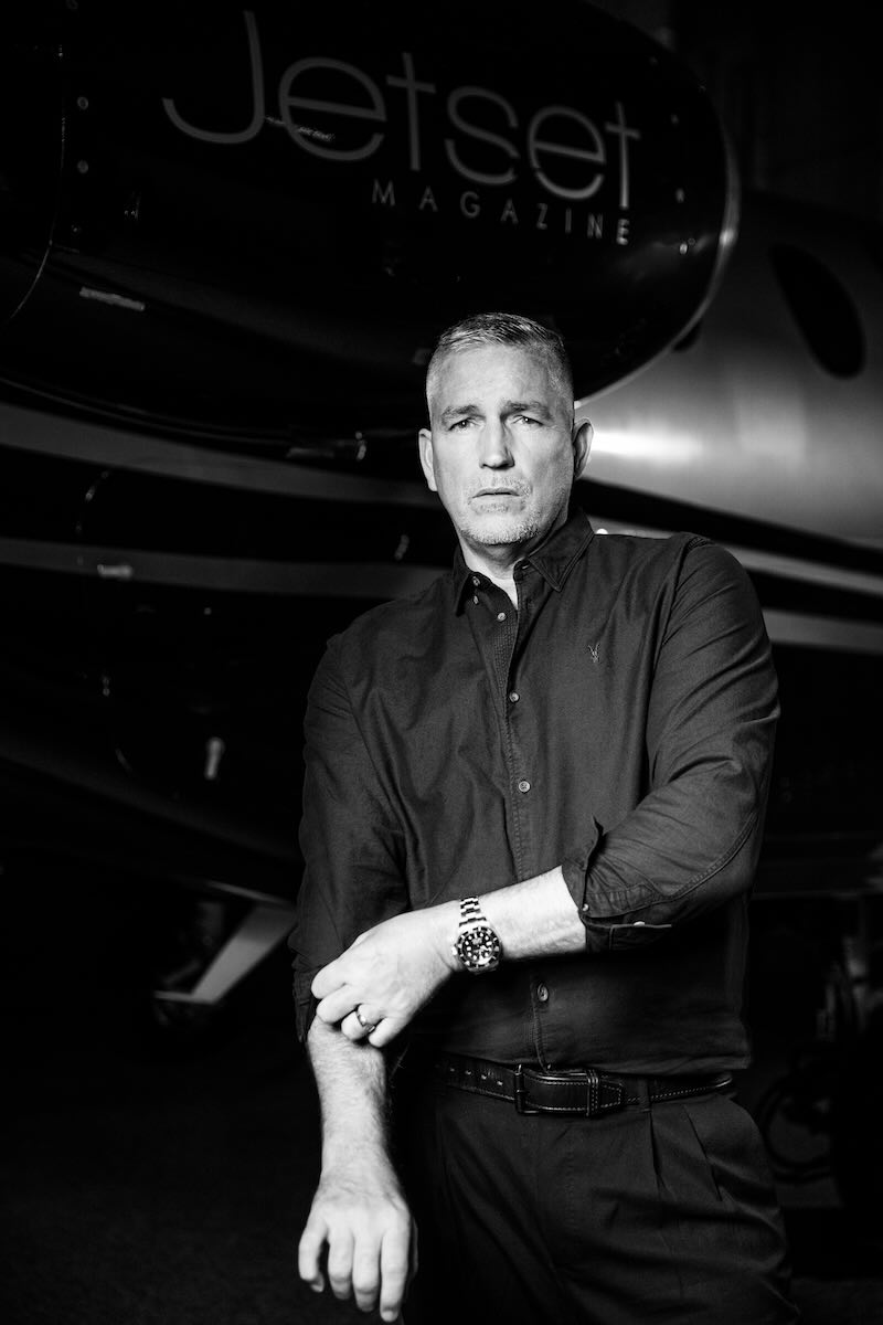 Jim Caviezel stands in front of Jetset's plane, rolling up his sleeve. 