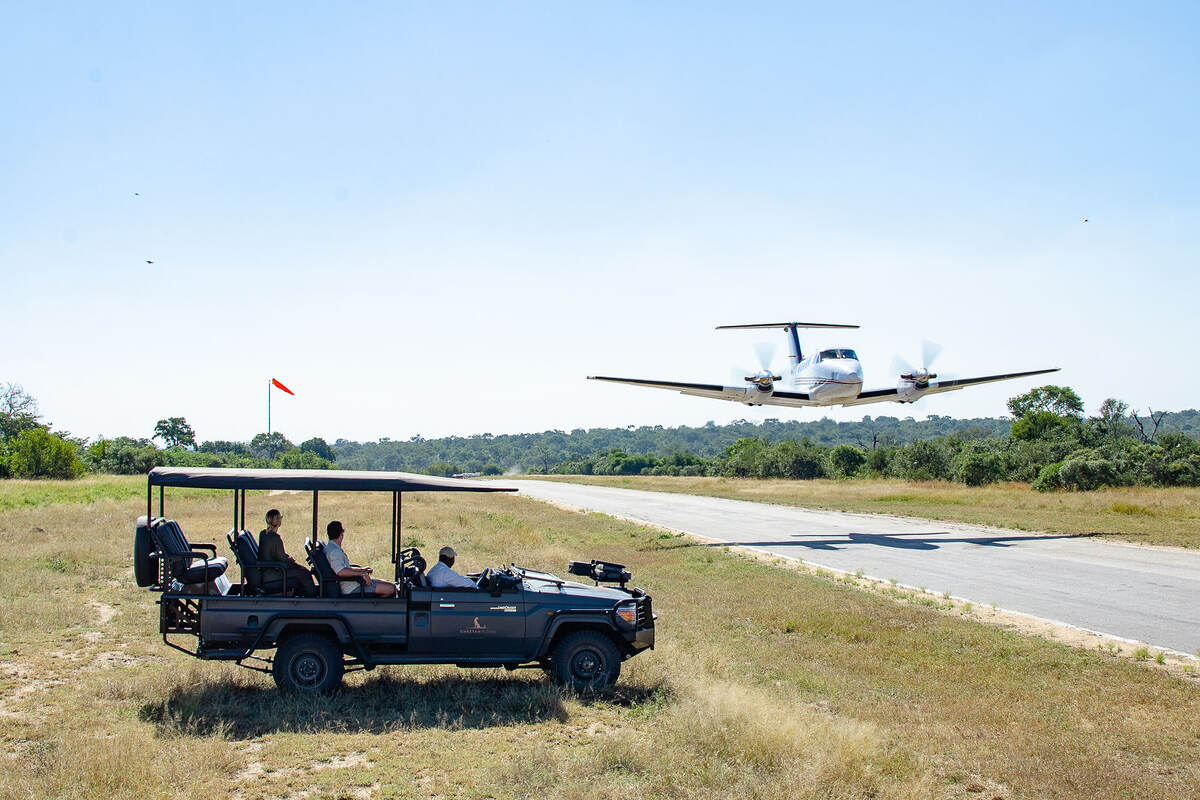 Airlpane landing while safari crew look on from a small vehicle. 